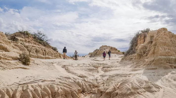 Four people walk through interesting rock formations in a desert scene