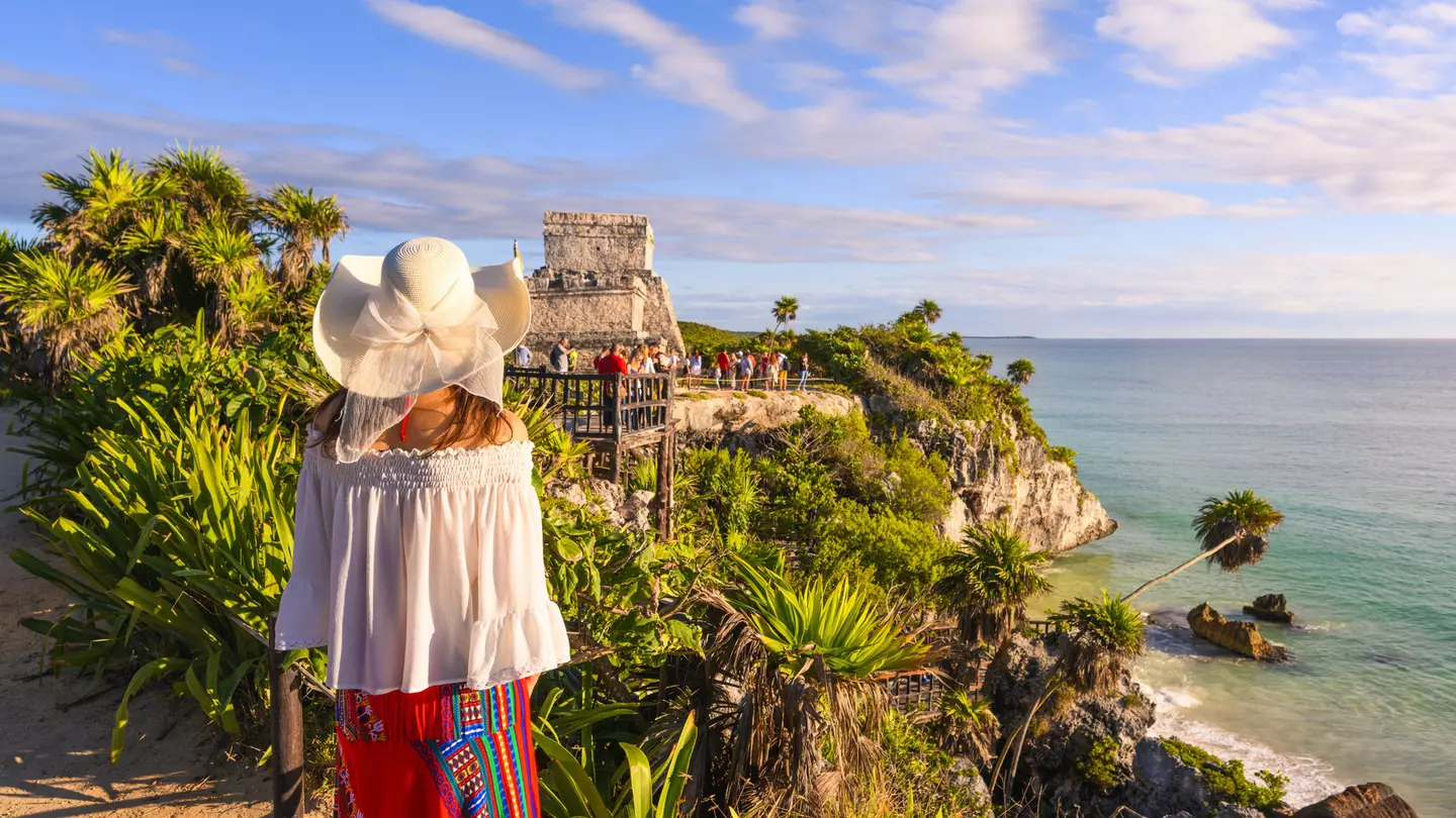 A woman stands on the cliffside admiring the Tulum ruins in Quintana Roo, Mexico