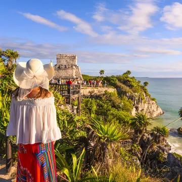 A woman stands on the cliffside admiring the Tulum ruins in Quintana Roo, Mexico