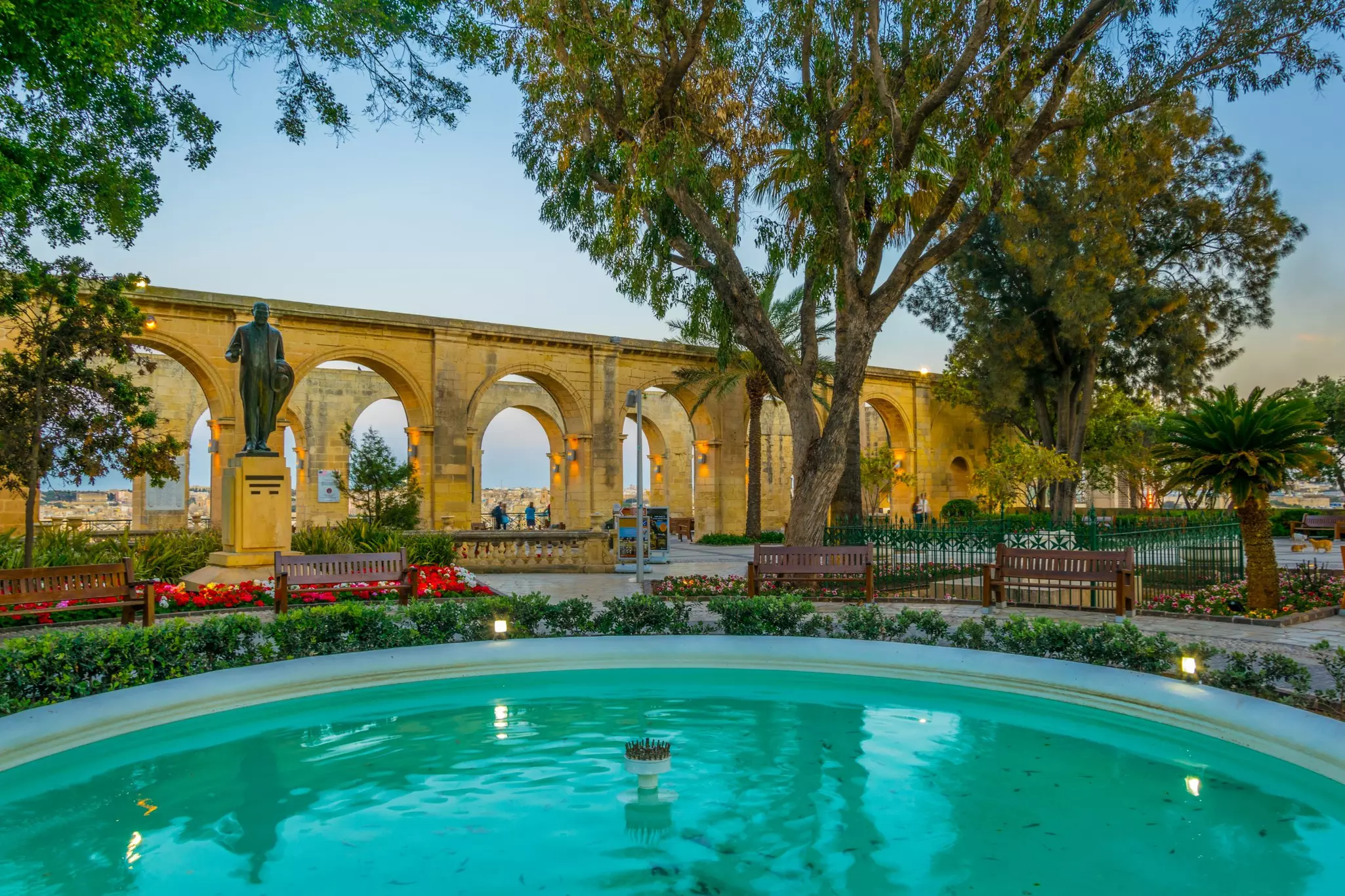 Sunset view of the Upper Barrakka Gardens with warm orange lights, red flowers and turquoise water