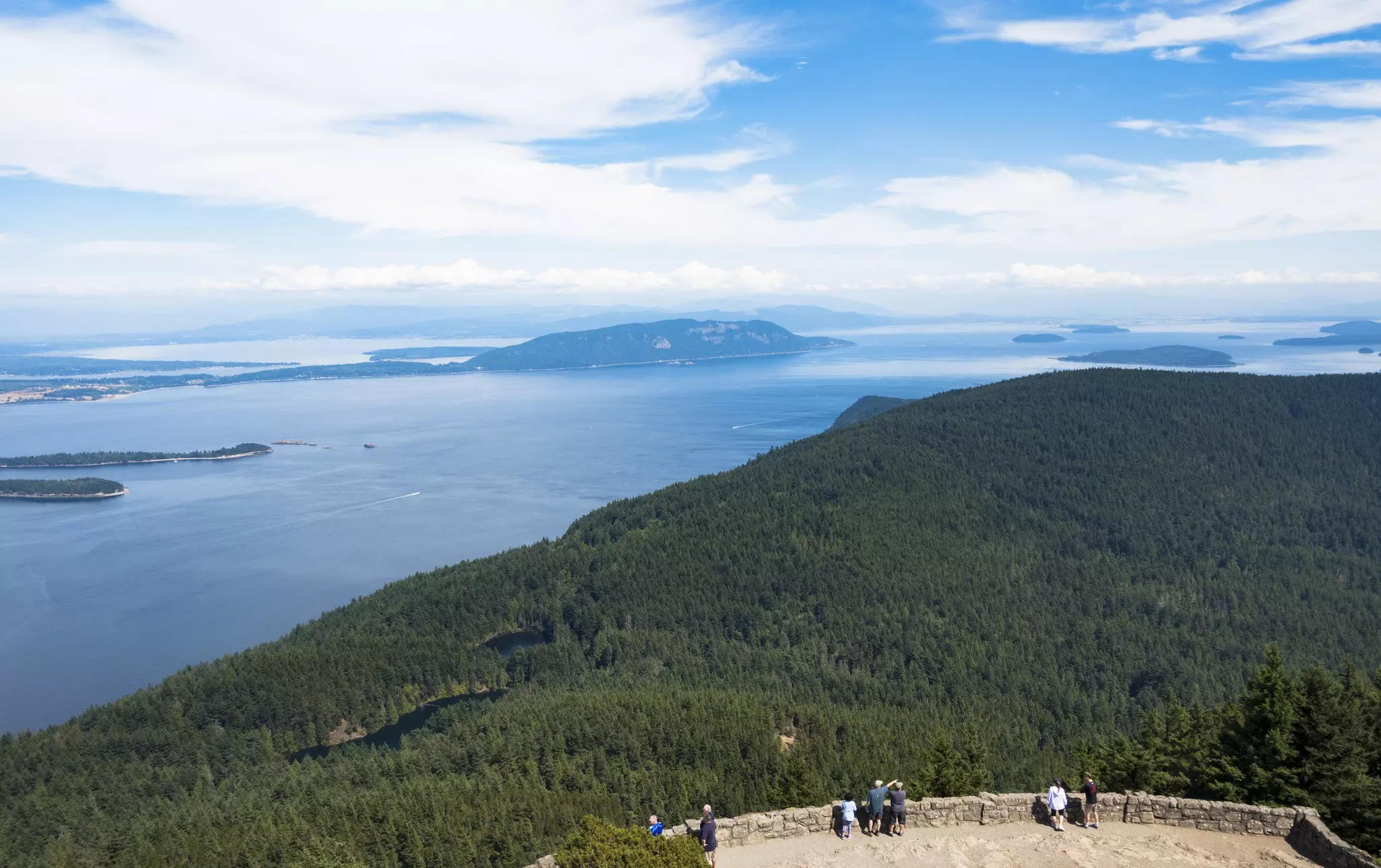 Hikers at a concrete viewing platform on an island high above dense woodland looking out at nearby islands.