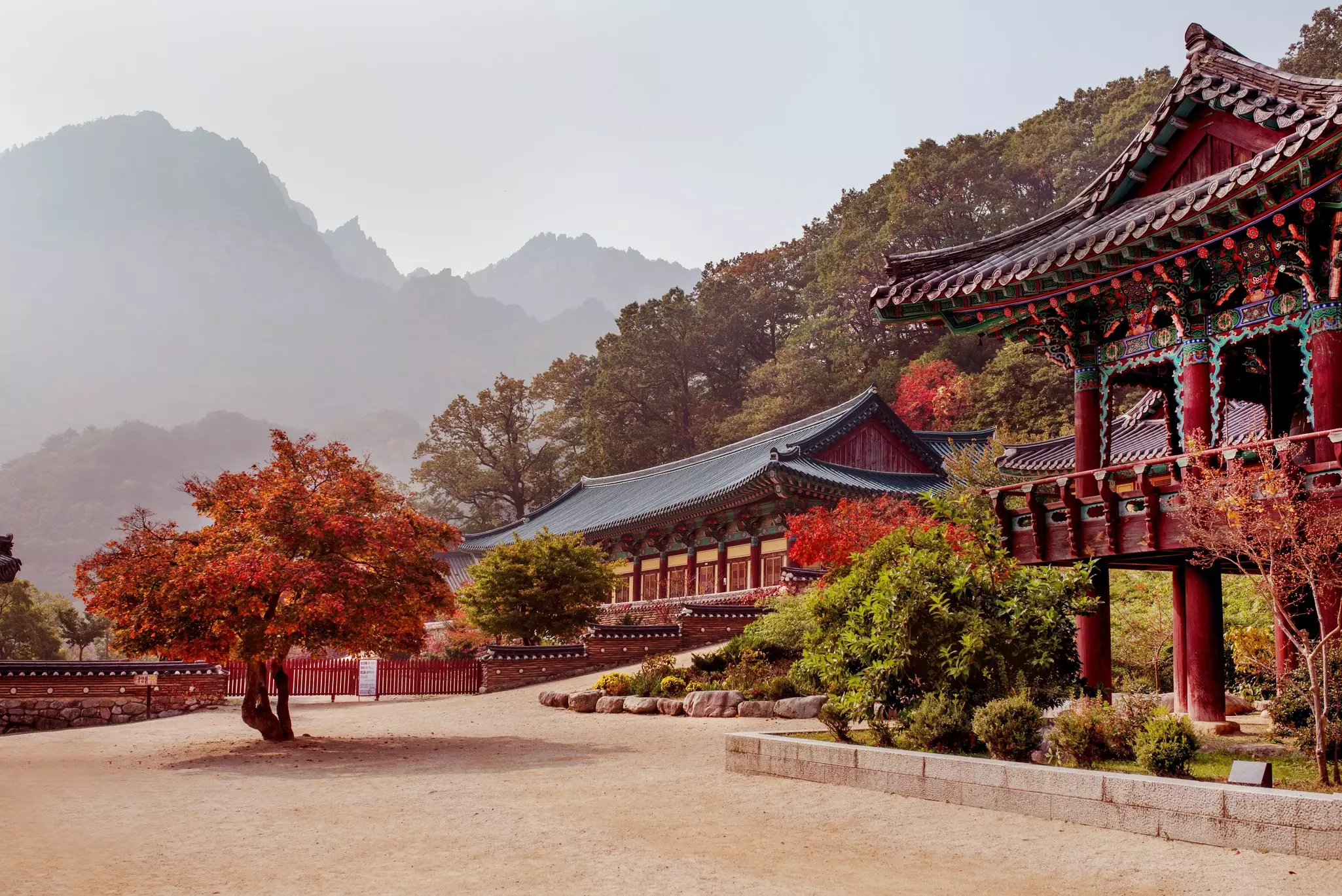 Low-rise temple buildings in a mountainous landscape surrounded by red foliage.