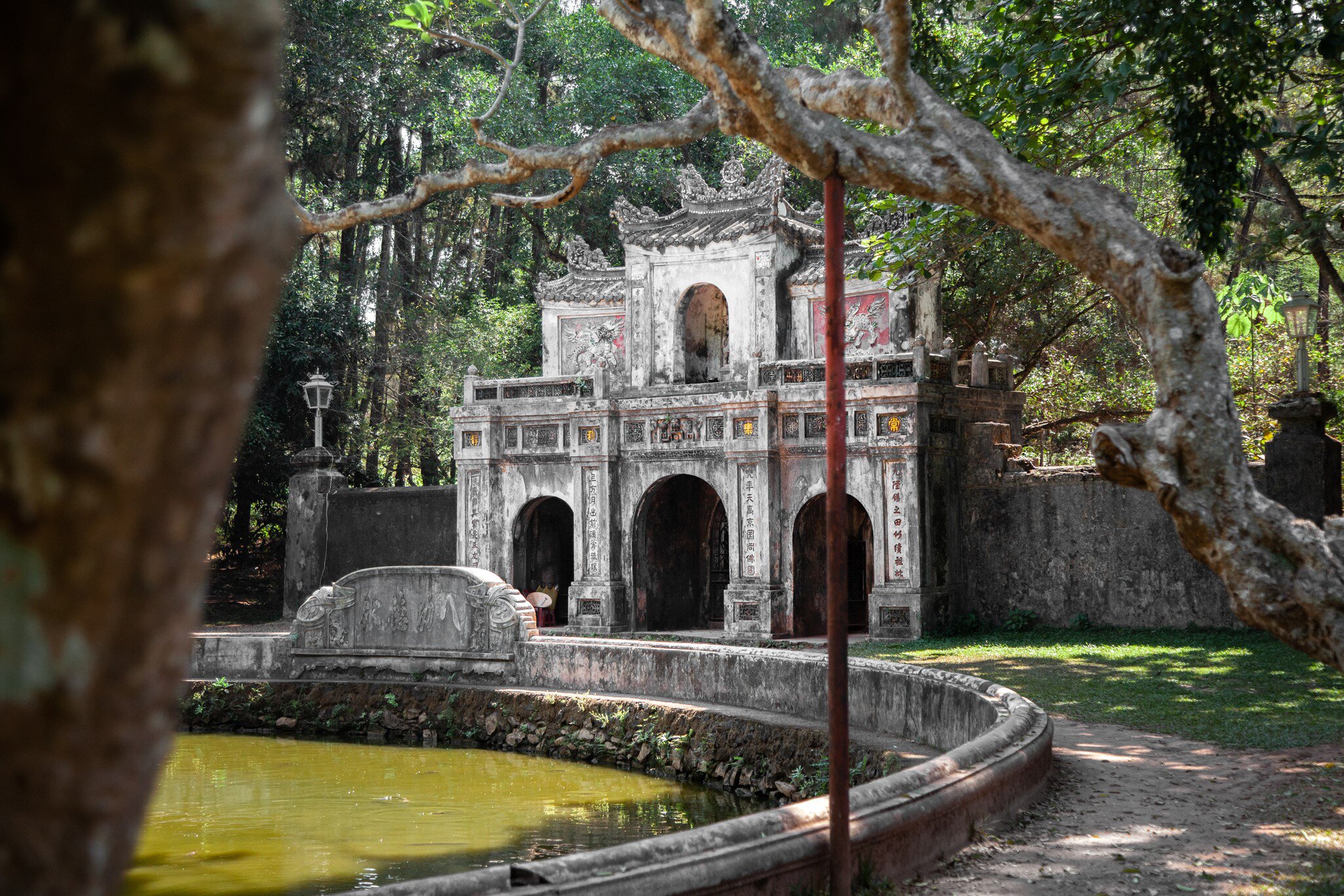The main stone gate of Hanh Tu Hieu pagoda, with lush green overhanging branches above and around it, in Hue City, central Vietnam.