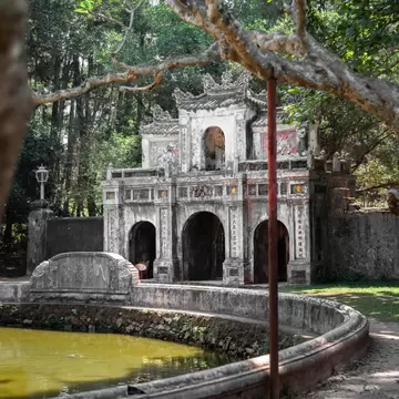 The main stone gate of Hanh Tu Hieu pagoda, with lush green overhanging branches above and around it, in Hue City, central Vietnam.