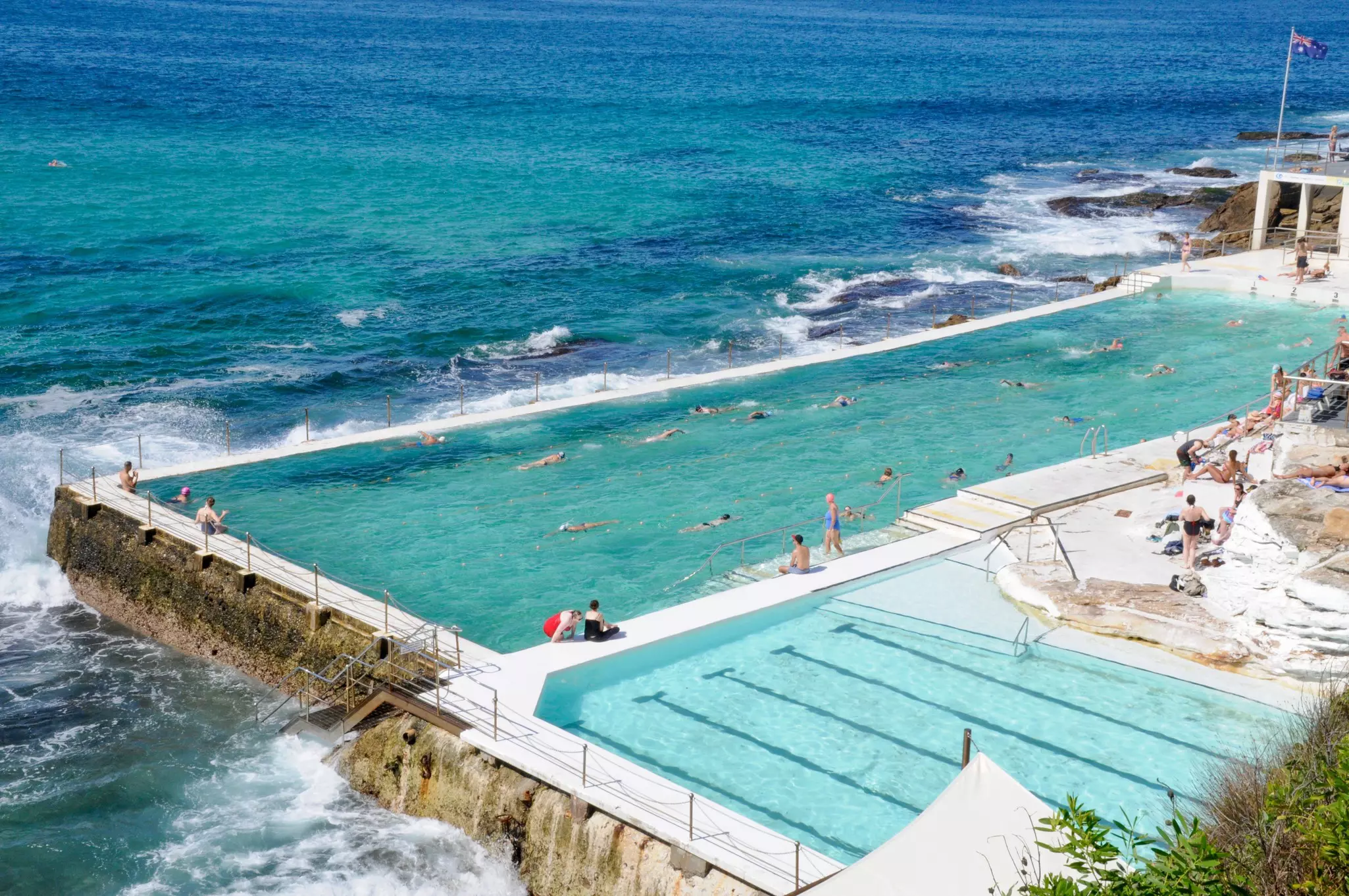 People swim in a manmade pool on the sea on Bondi Beach on a sunny day