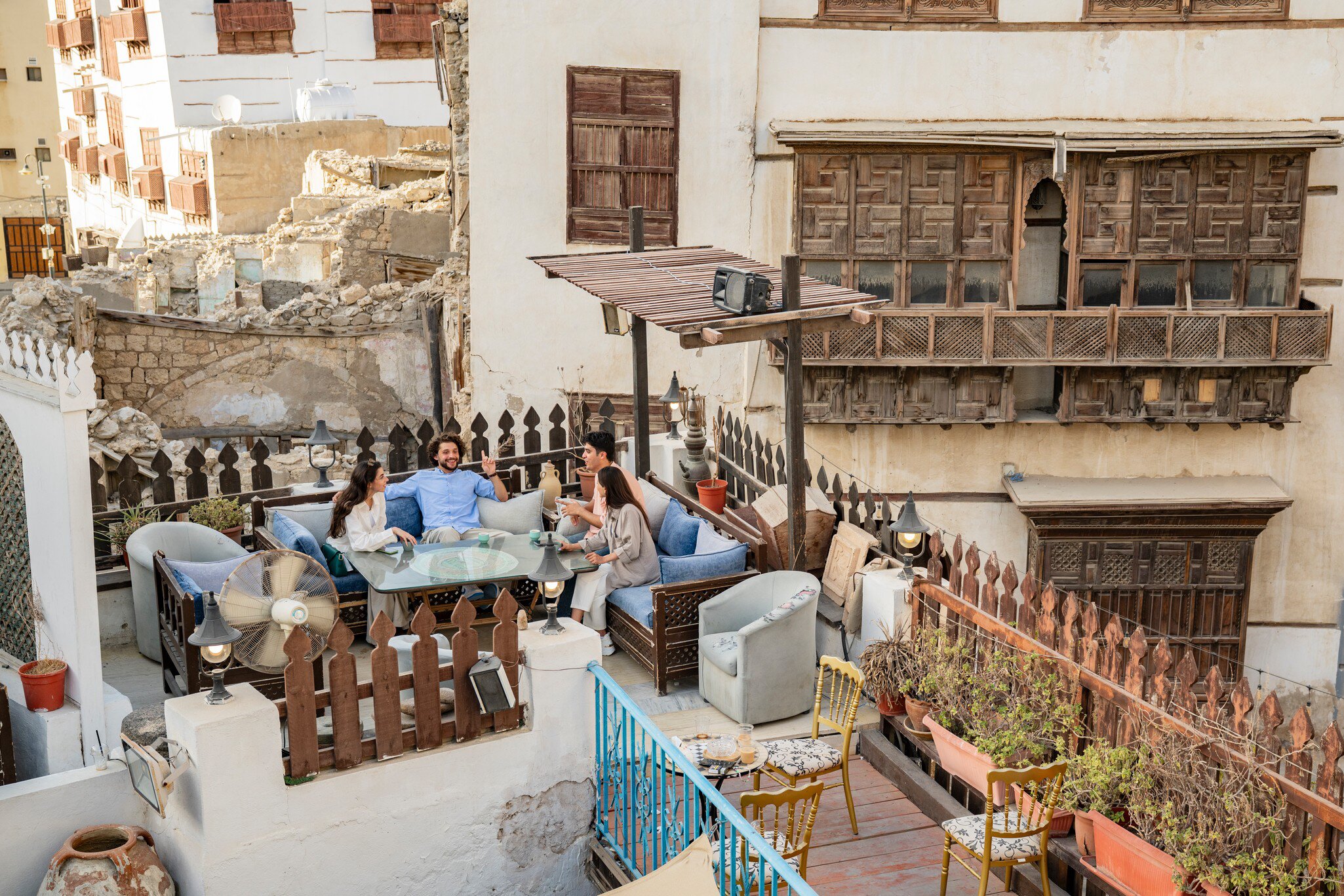 Friends chat on a rooftop terrace beside carved wooden roshan balconies of old coral-stone houses in Al-Balad, Jeddah