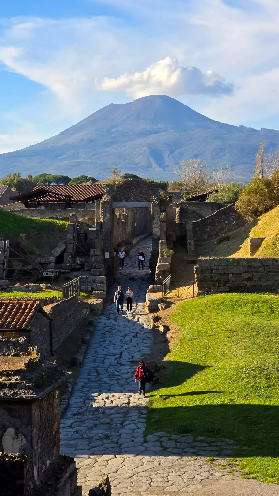 Path through Pompei with Mount Vesuvius in the distance under a blue sky with cloud