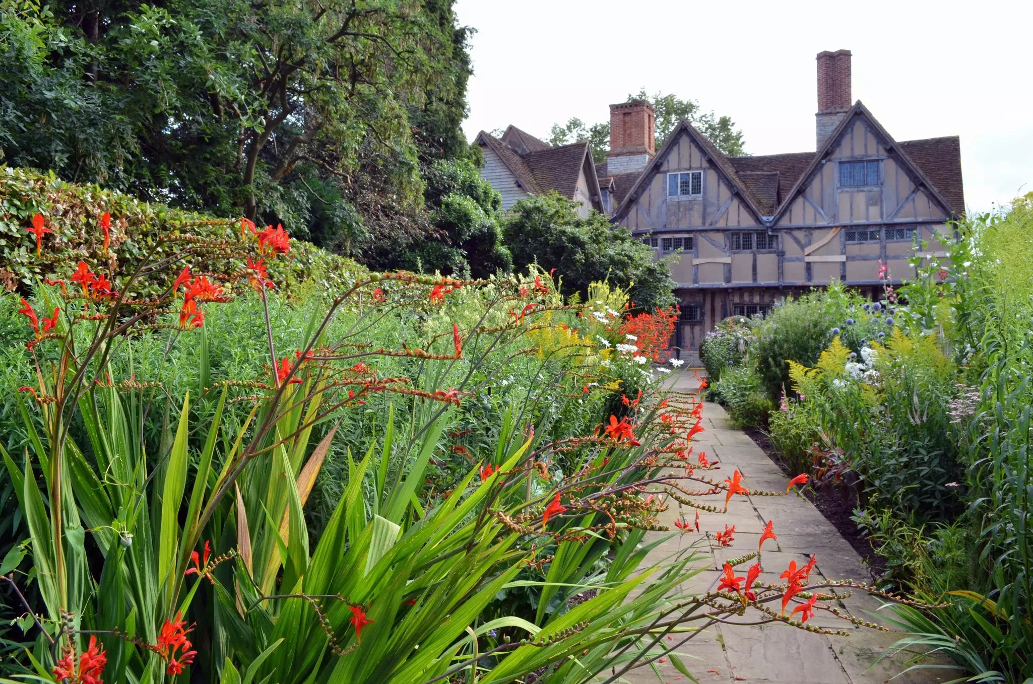 A red-brick Tudor house surrounded by gardens in full bloom
