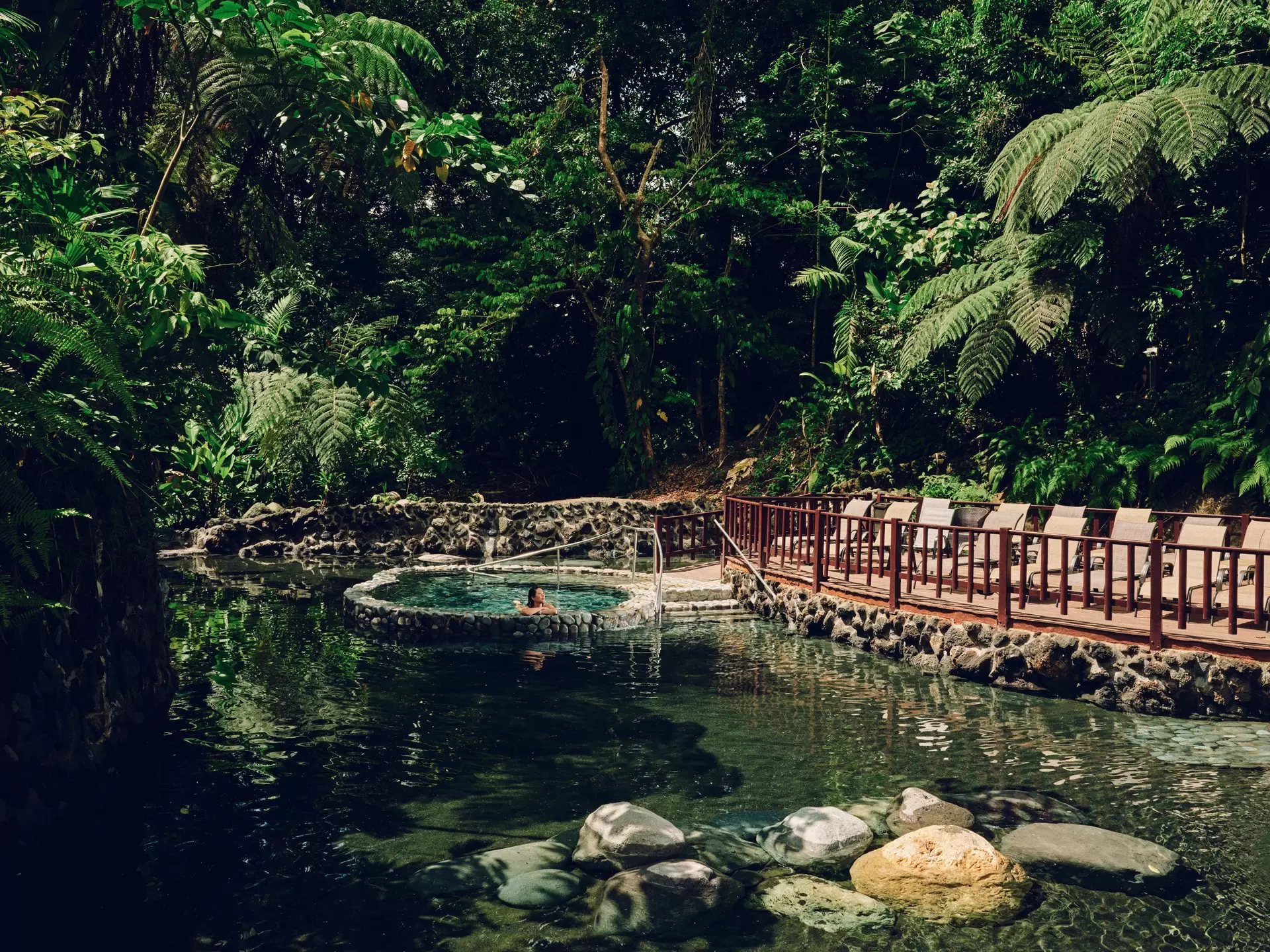 A woman sitting alone in a hot spring pool clad in stones surrounded by forest