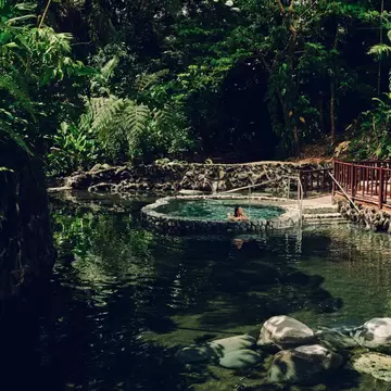 A woman sitting alone in a hot spring pool clad in stones surrounded by forest