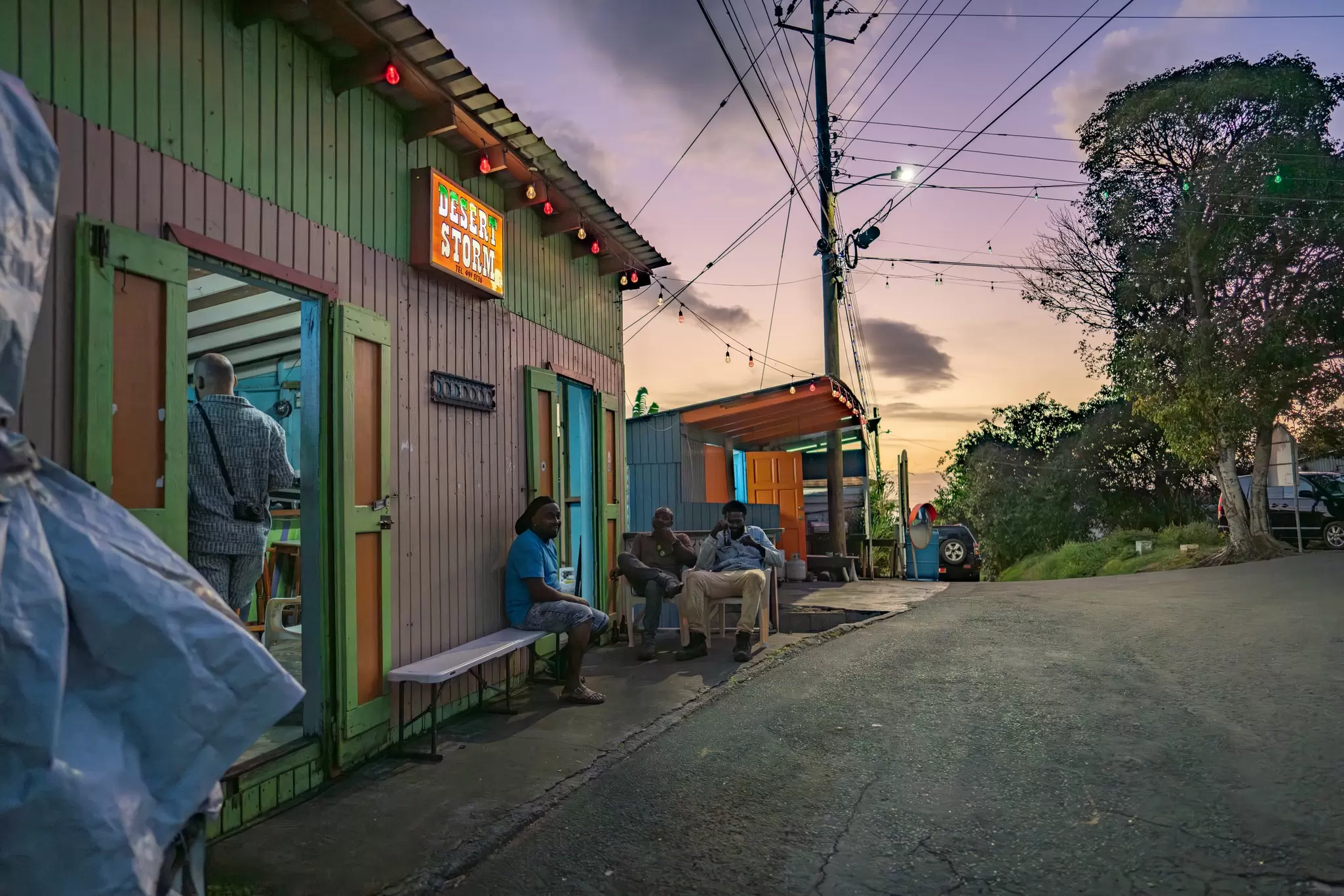 Exterior of a colorful rum shop in Salem run by Miga Graham with the sun setting beyond