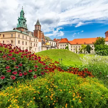 Colorful flower beds in front of a castle's towers and terracotta roofs.