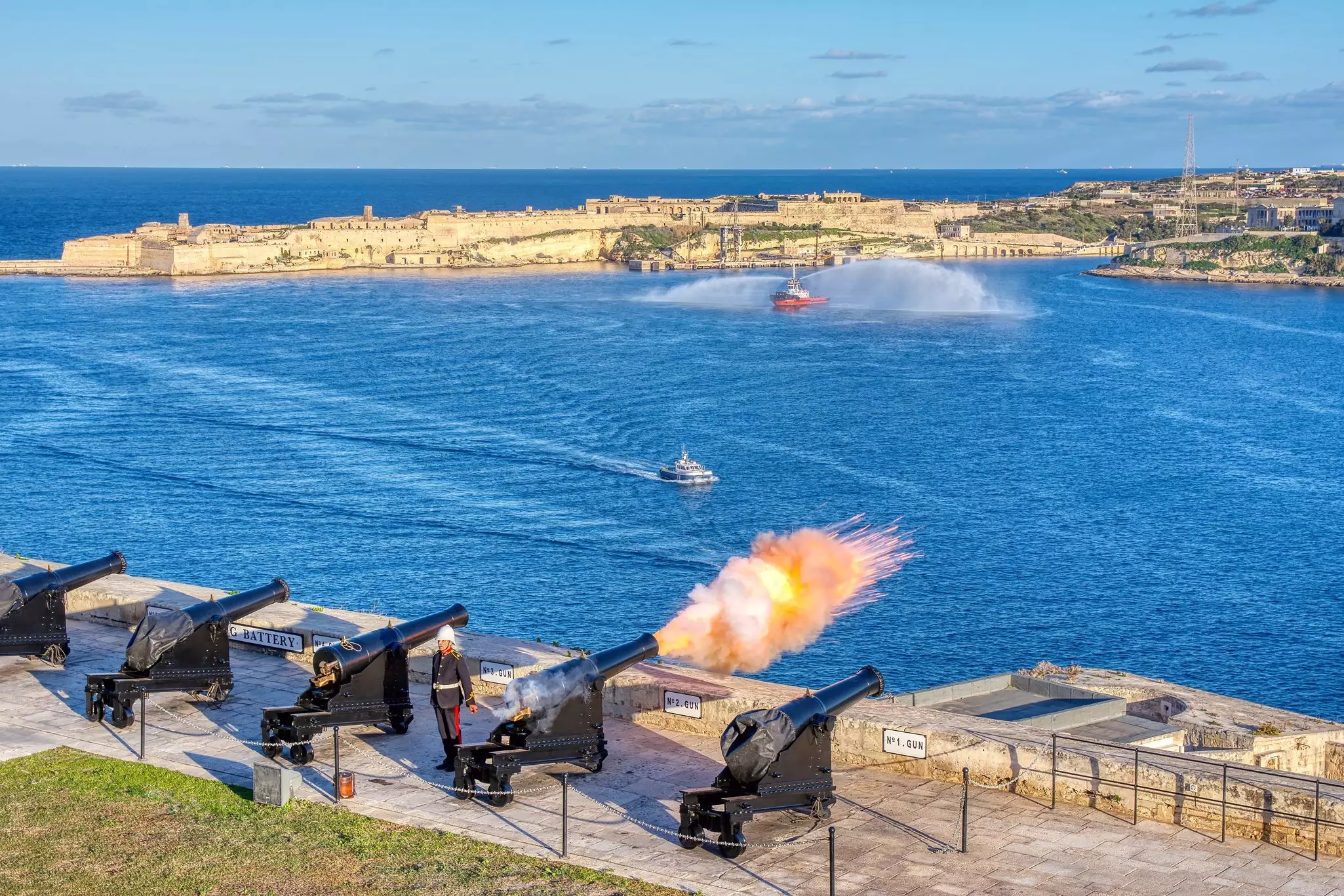 A cannon fires at noon from the Saluting Battery in Valletta, Malta, with Birgu in the background.
