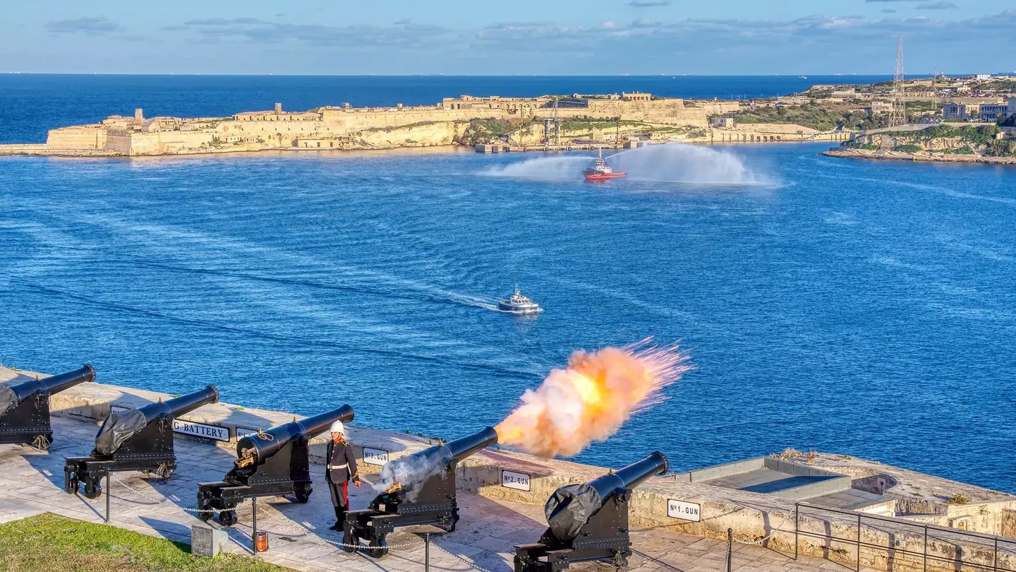 A cannon fires at noon from the Saluting Battery in Valletta, Malta, with Birgu in the background.
