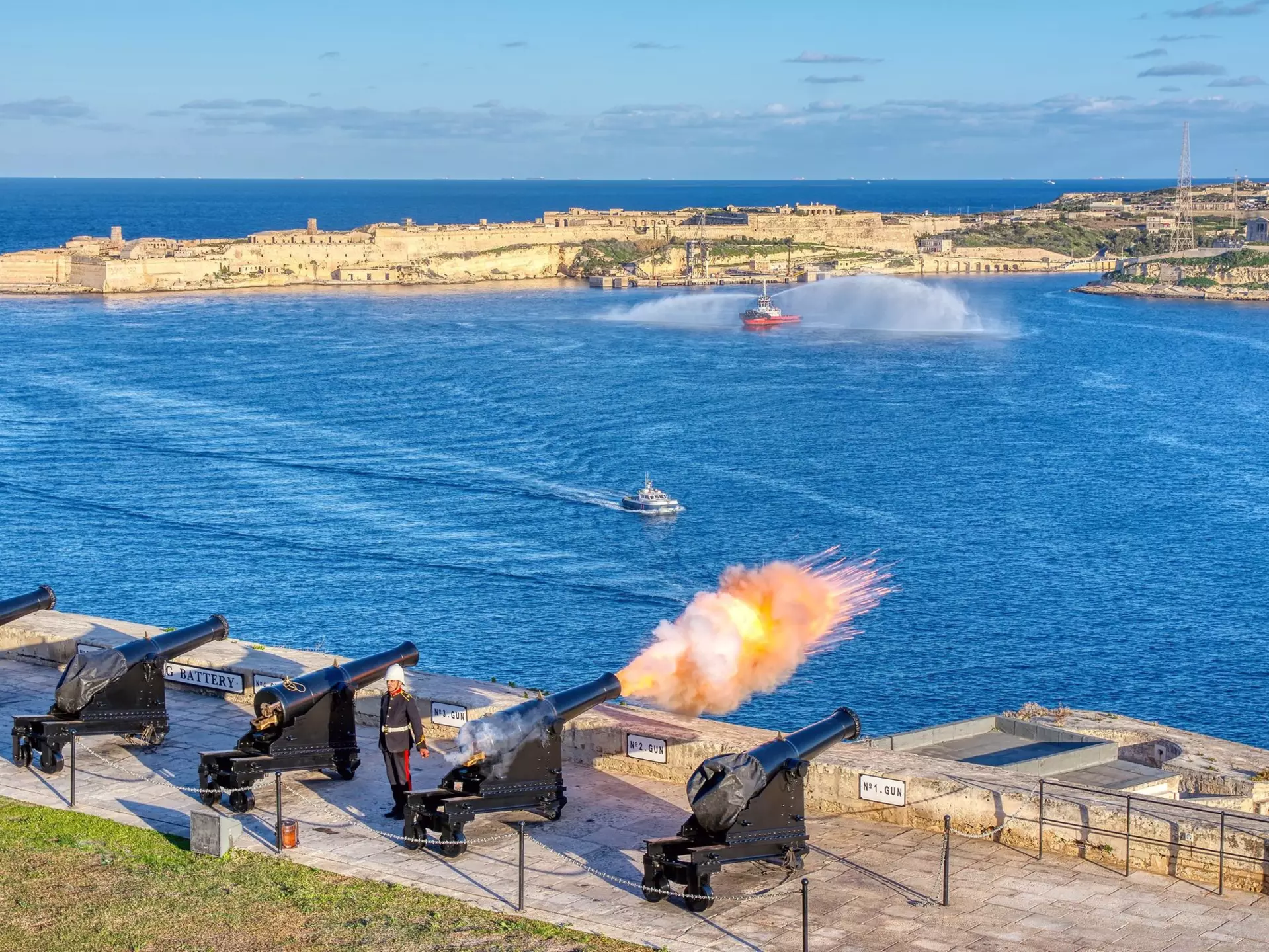A cannon fires at noon from the Saluting Battery in Valletta, Malta, with Birgu in the background.