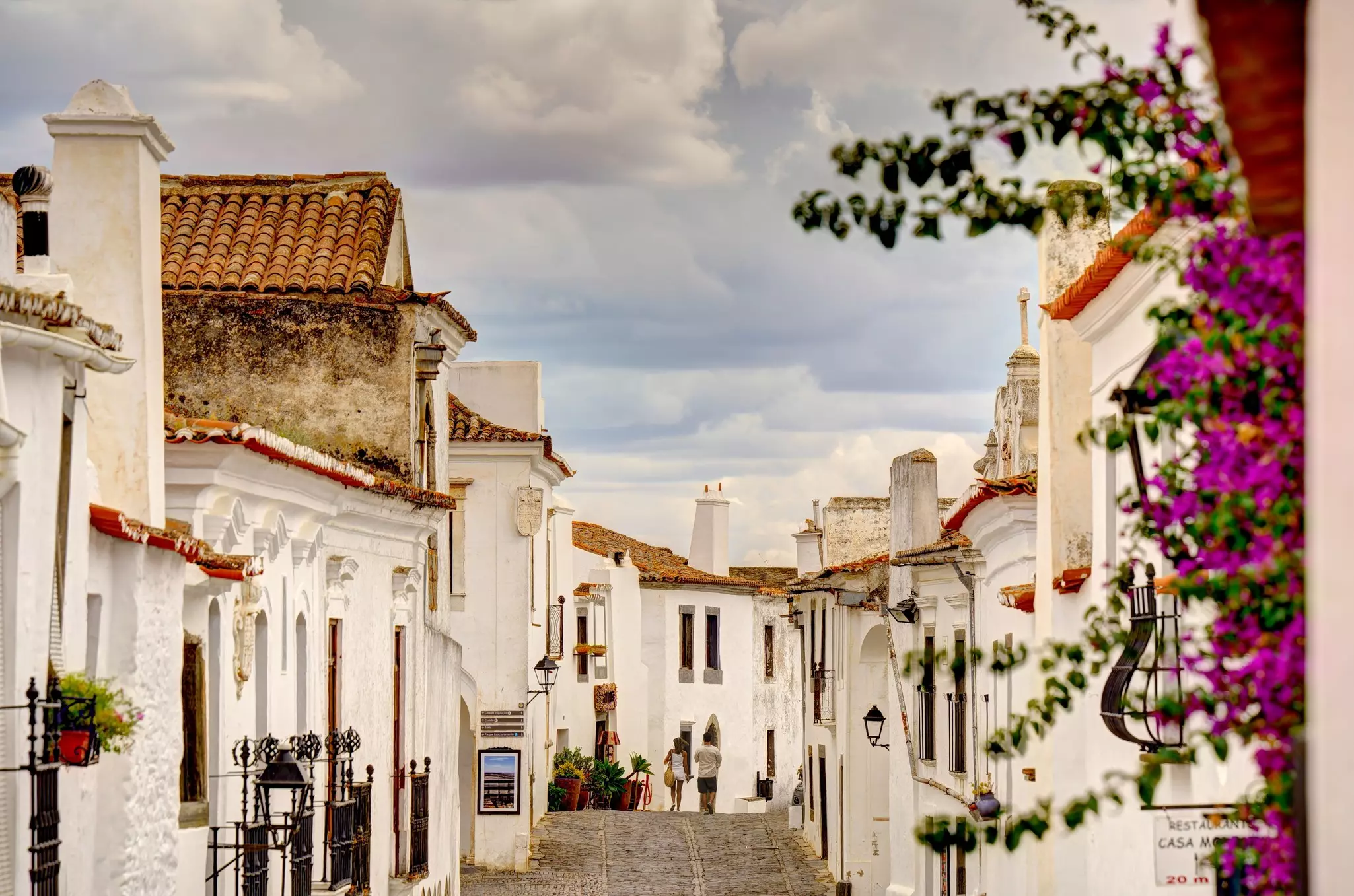 People walk down the cobbled lane of a hilltop town with whitewashed buildings 