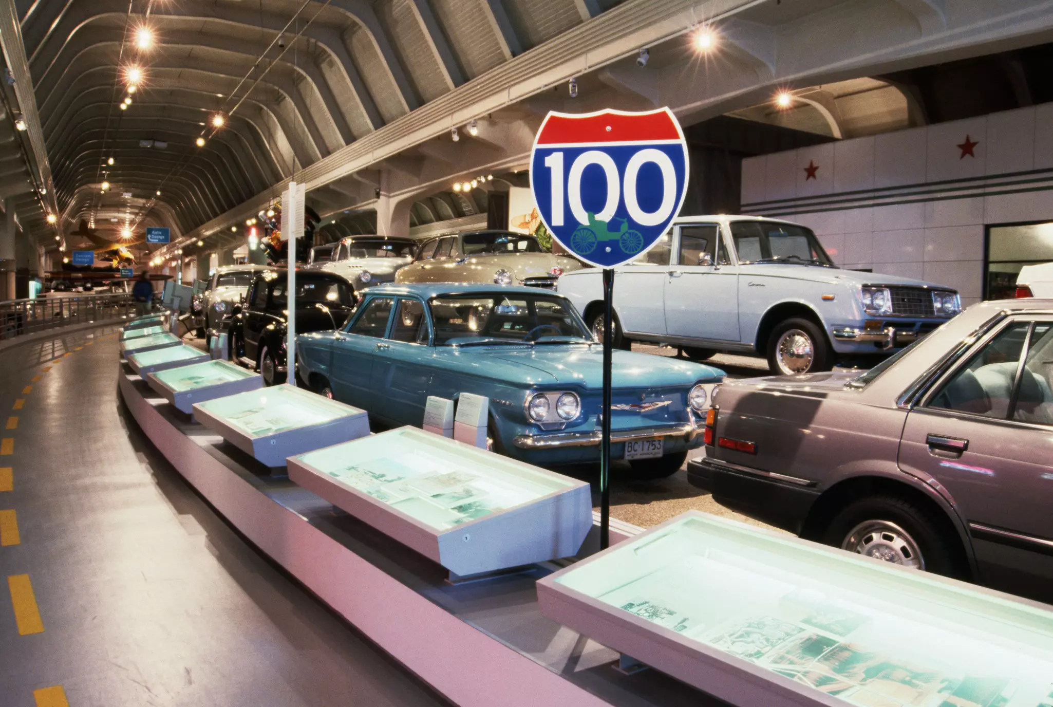 Cars from different decades lined up in a museum that resembles an automotive tunnel.