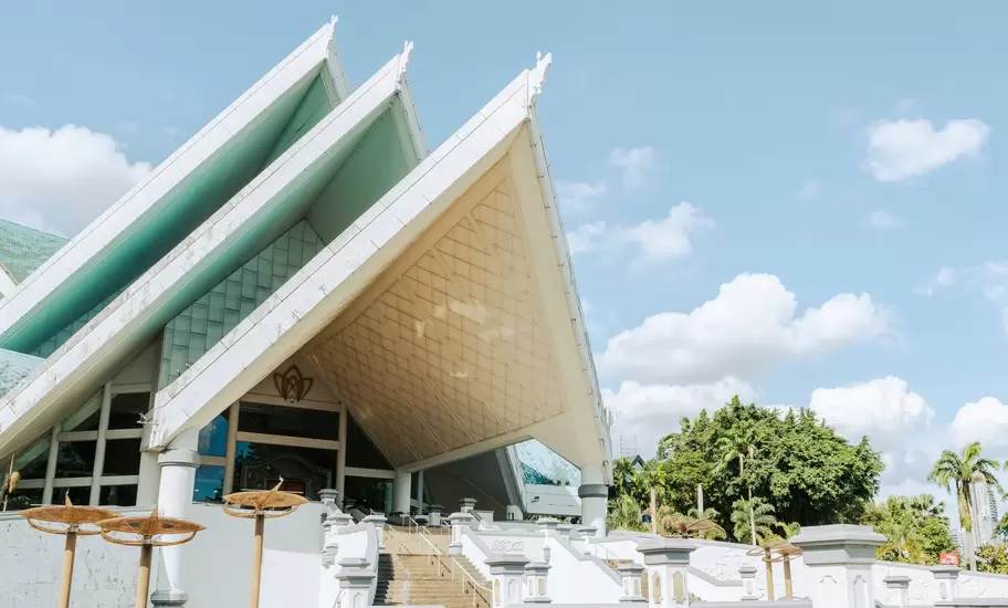 Pointed white-and-green tiered roofs of Istana Budaya in Kuala Lumpur, with entrance steps and palm trees