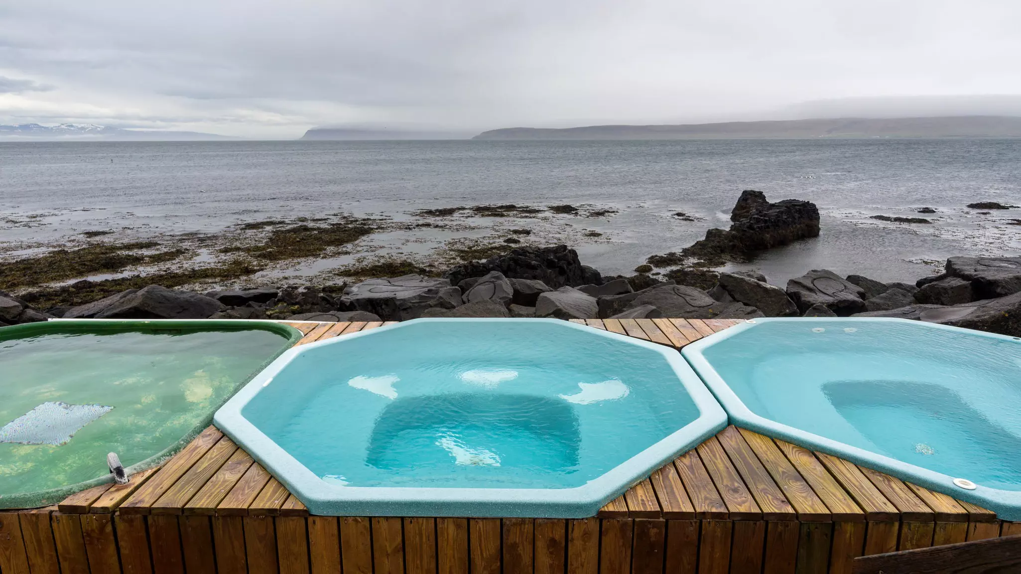 A row of three hot tubs on the rocky shore
