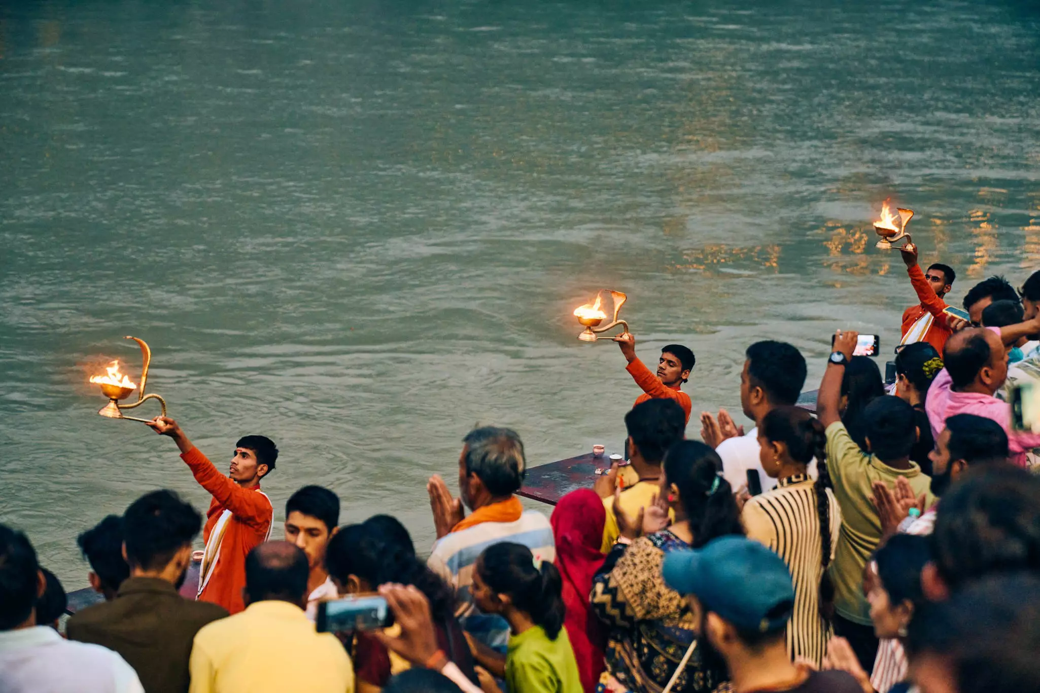 A crowd of people watch a Hindu ritual with lamps of fire on a river bank