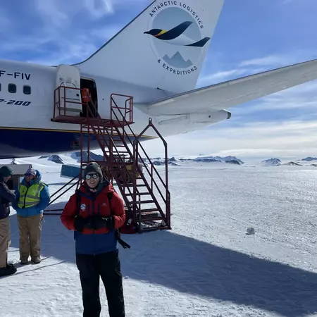 A woman stands in front of the exit stairs from a large commercial airliner on a runway of ice.