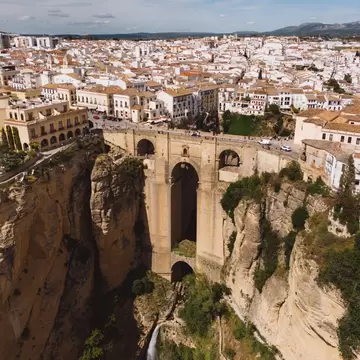 Stone arches of Ronda's Puente Nuevo span a deep gorge with a waterfall below, whitewashed town spreading behind
