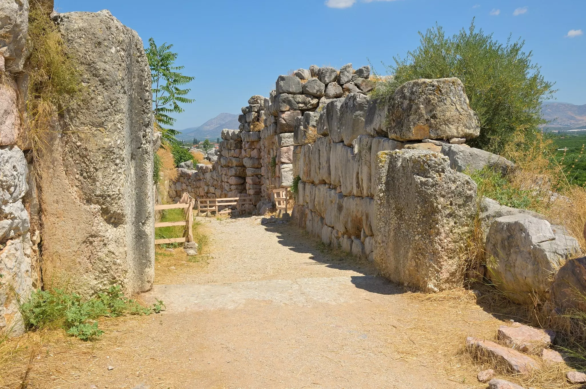 A path leads by thick stone walls at an archaeological site.