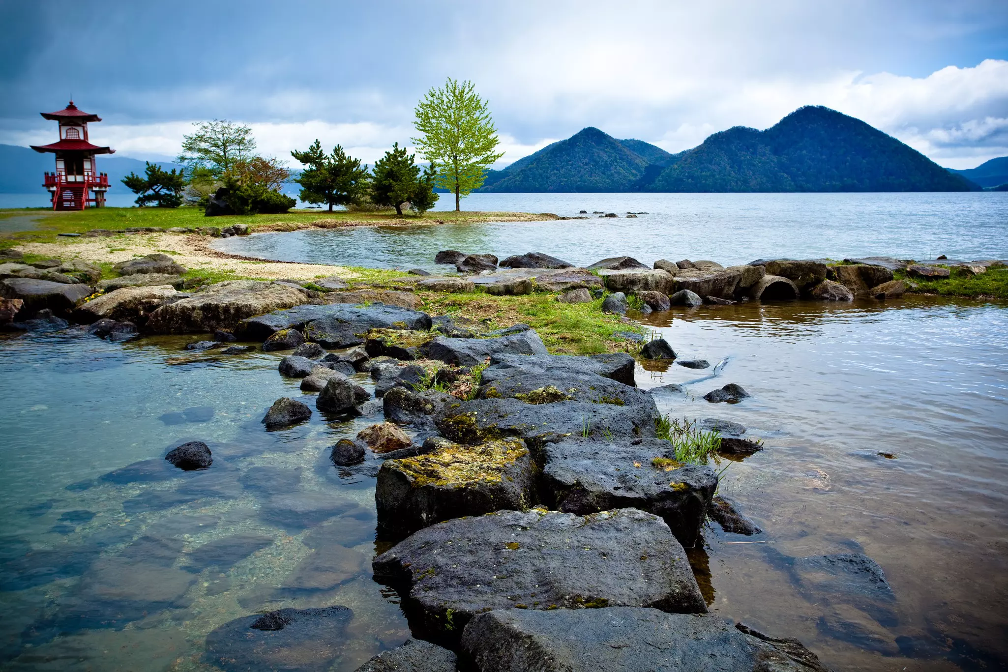 Rocks in a lake, with a red temple to the left and hills on the distant shore.