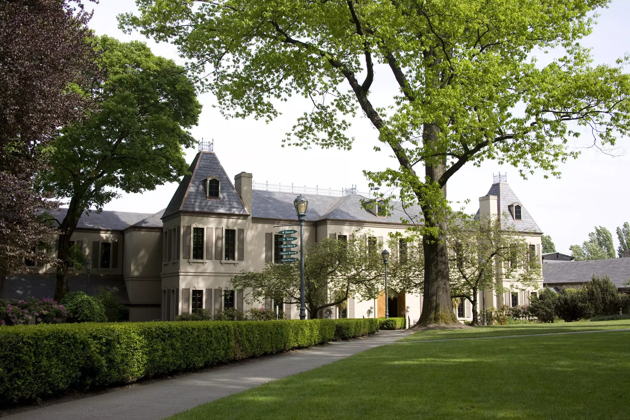 Exterior of a large chateau surrounded by a groomed yard with large trees in front
