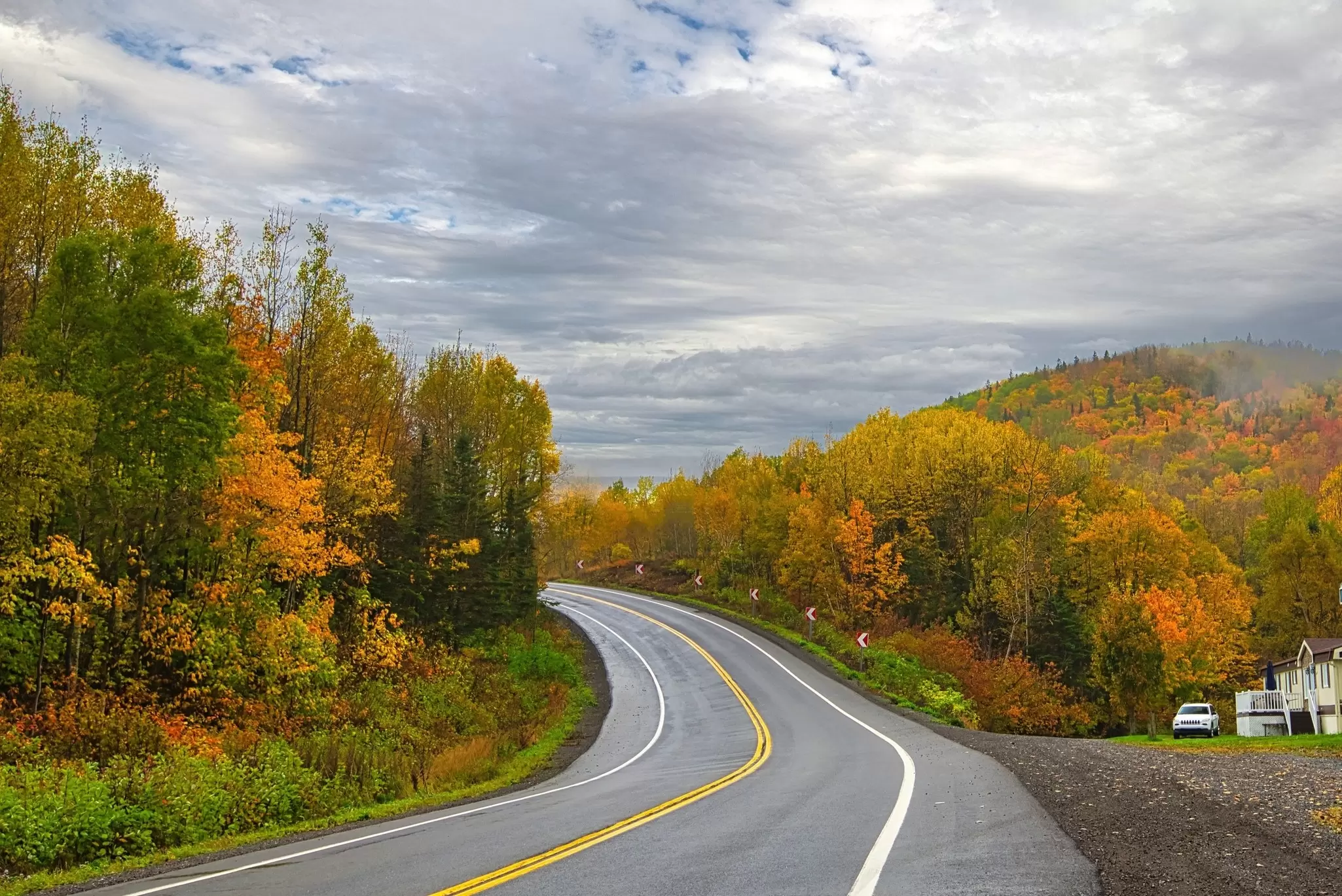 A highway leads through a stretch of hilly countryside with trees in fall foliage in the Gaspésie Peninsula, Québec, Canada.