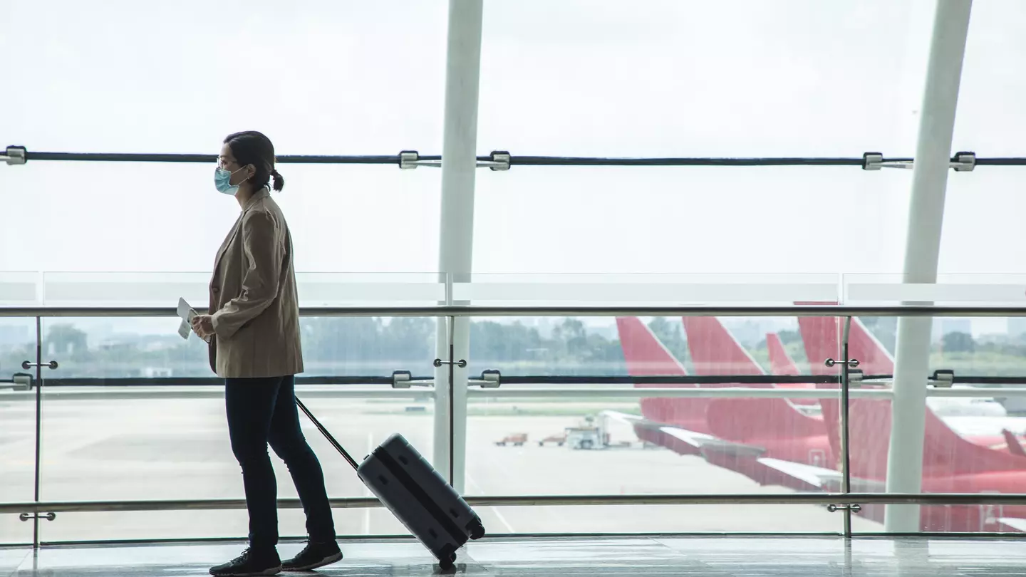 Asian businesswoman wearing a mask at the airport with passport and airplane ticket in her hand