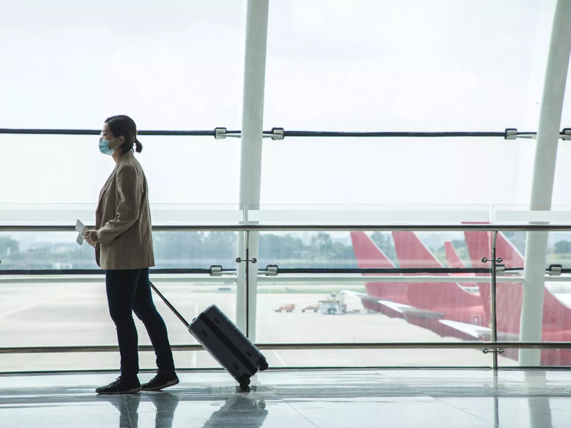 Asian businesswoman wearing a mask at the airport with passport and airplane ticket in her hand