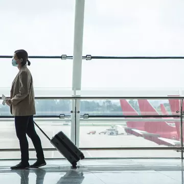 Asian businesswoman wearing a mask at the airport with passport and airplane ticket in her hand