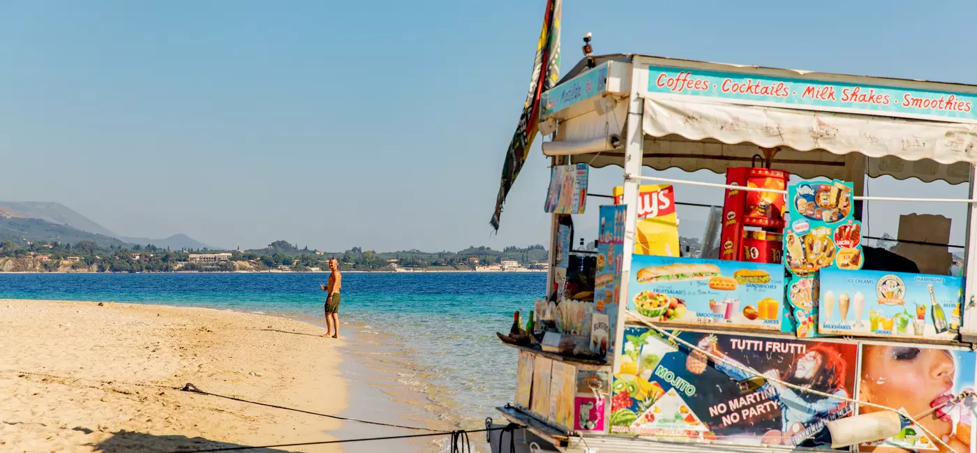 A boat selling snacks and drinks docked on a sandy beach.