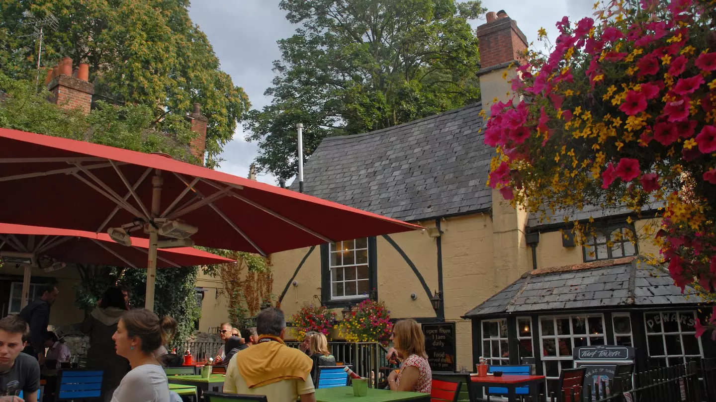 People enjoy drinks at outdoor tables in the beer garden of the Turf Tavern pub, Oxford, Oxfordshire, England, United Kingdom