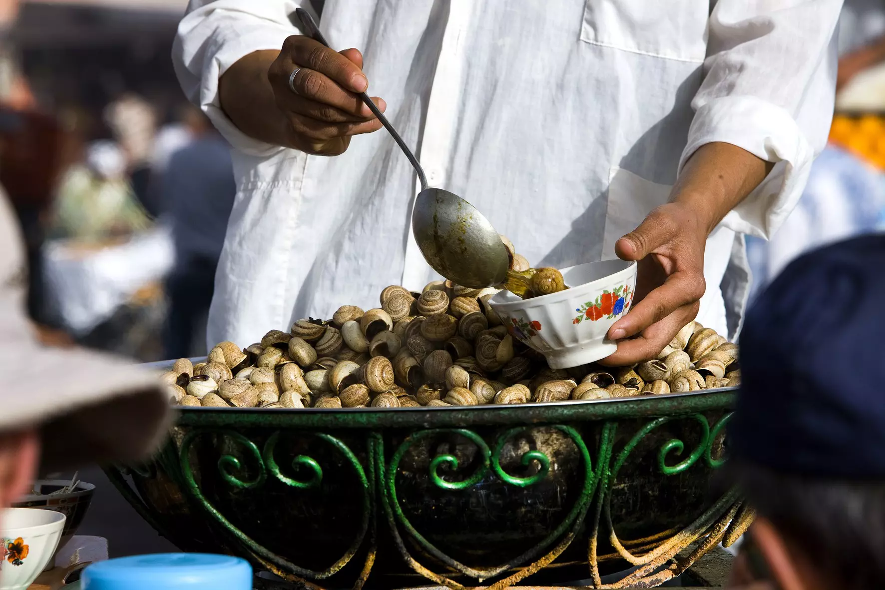 A man serves cooked snails in a bowl in a Marrakesh market.