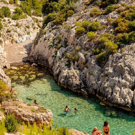 People swimming in the clear, almost green waters of a bay in Zakynthos.