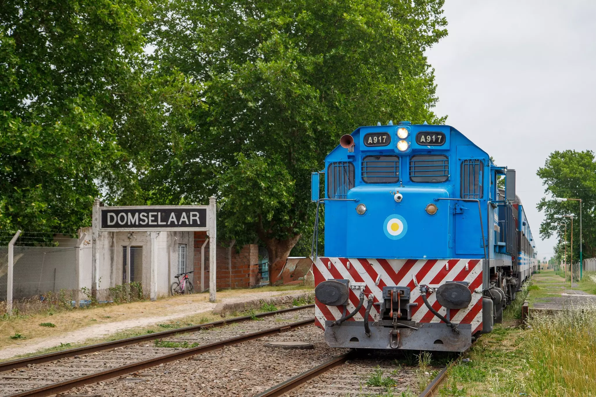 A large blue train engine standing still on rail tracks at a rural station.