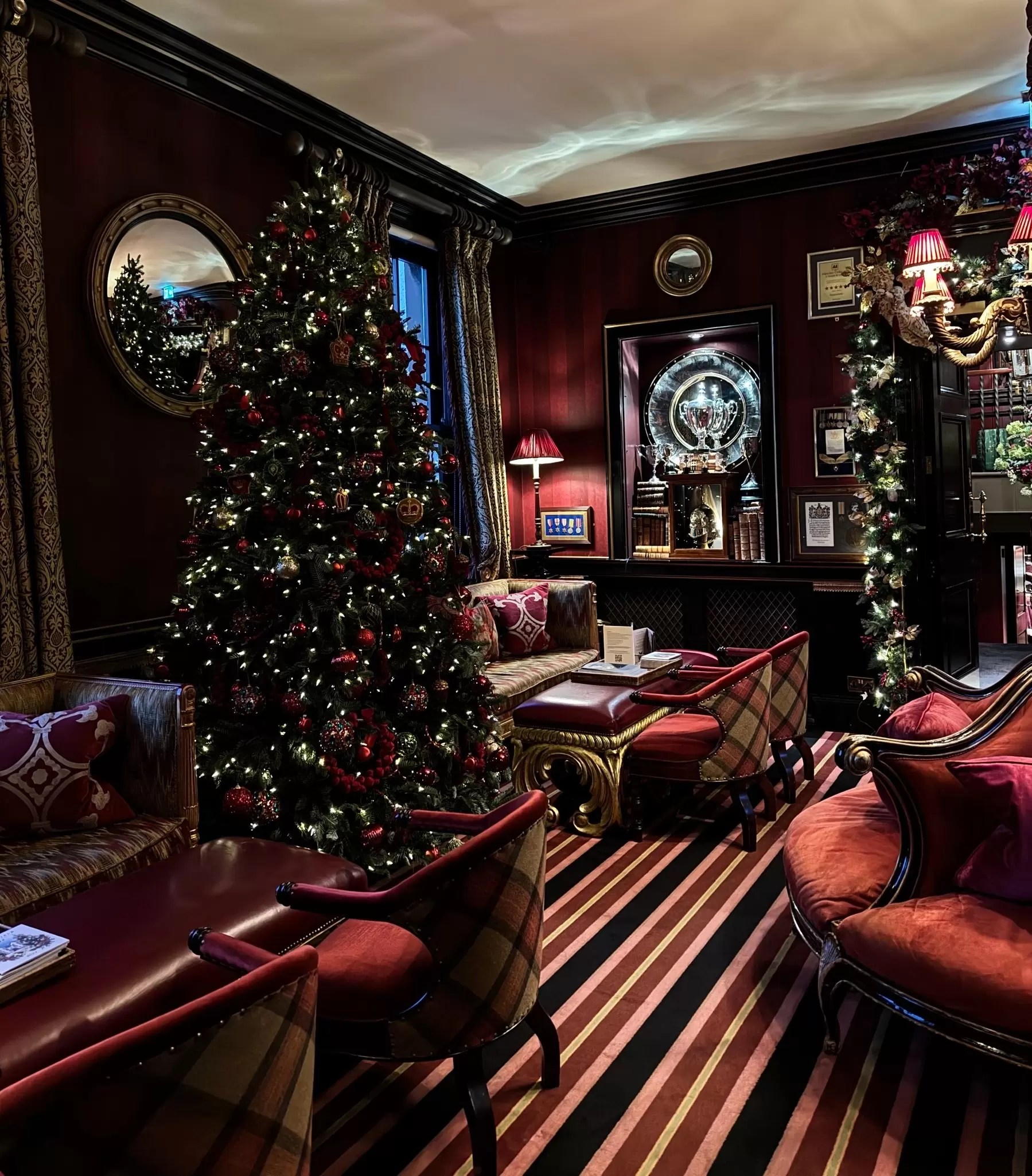 A cozy festive hotel lobby with plush red furniture, a tall lit-up Christmas tree and lit up garland stung around the doorway