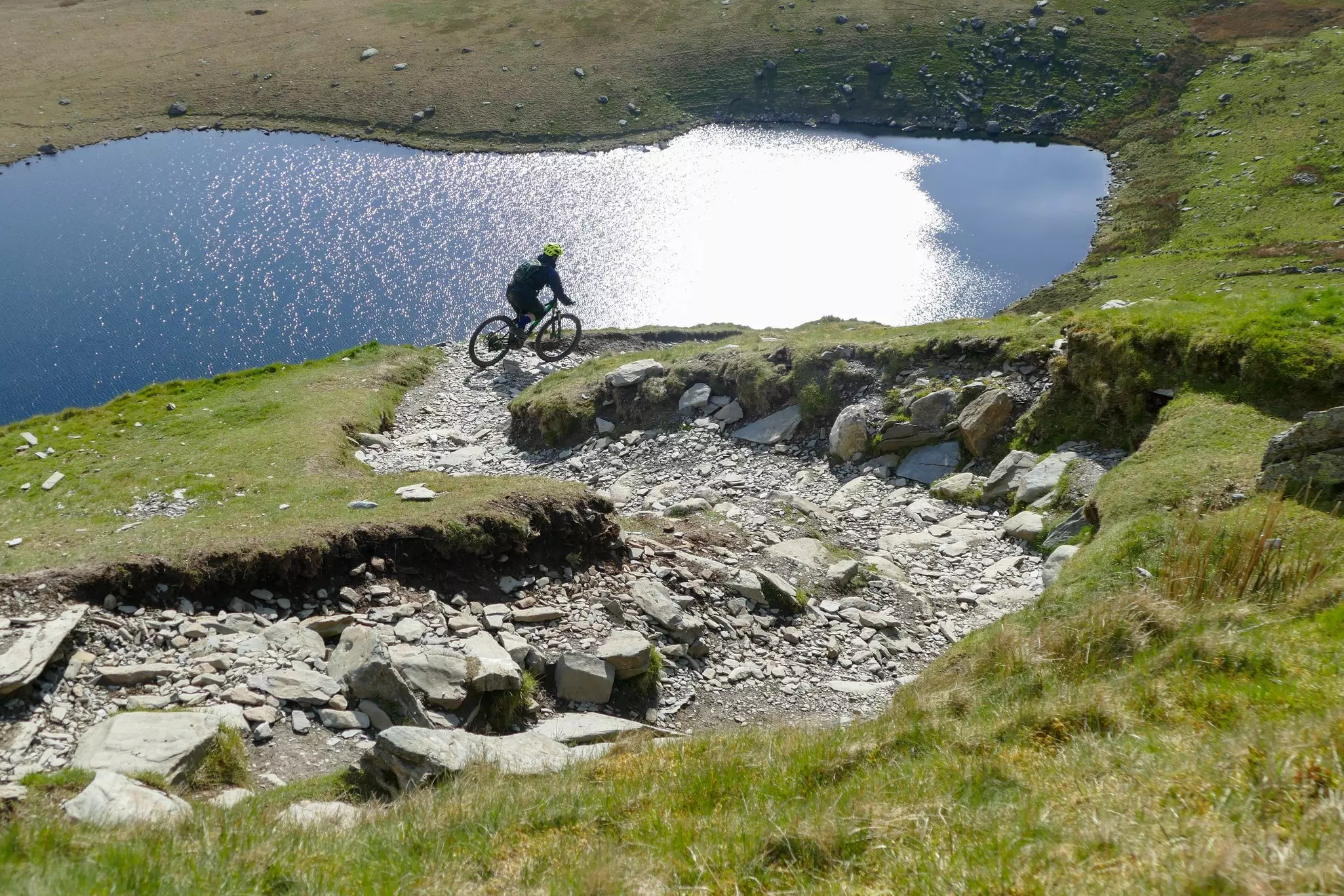 Downhill mountain biker above a glacial lake in Snowdonia, Wales.