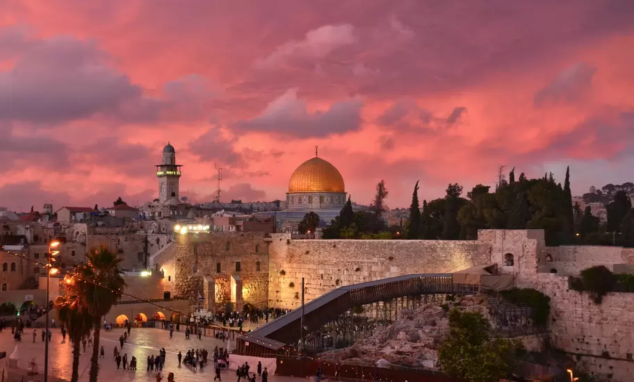 Jerusalem: Western Wall plaza with the gold Dome of the Rock and a minaret above, under a pink sunset sky