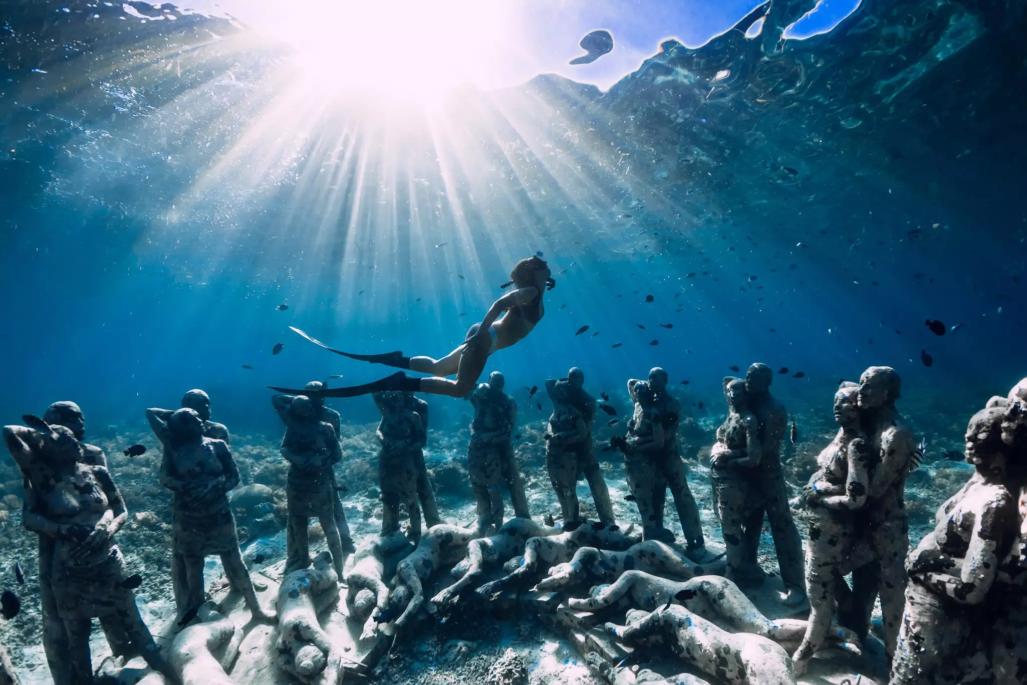 A snorkeler dives underwater past a circle of statues.