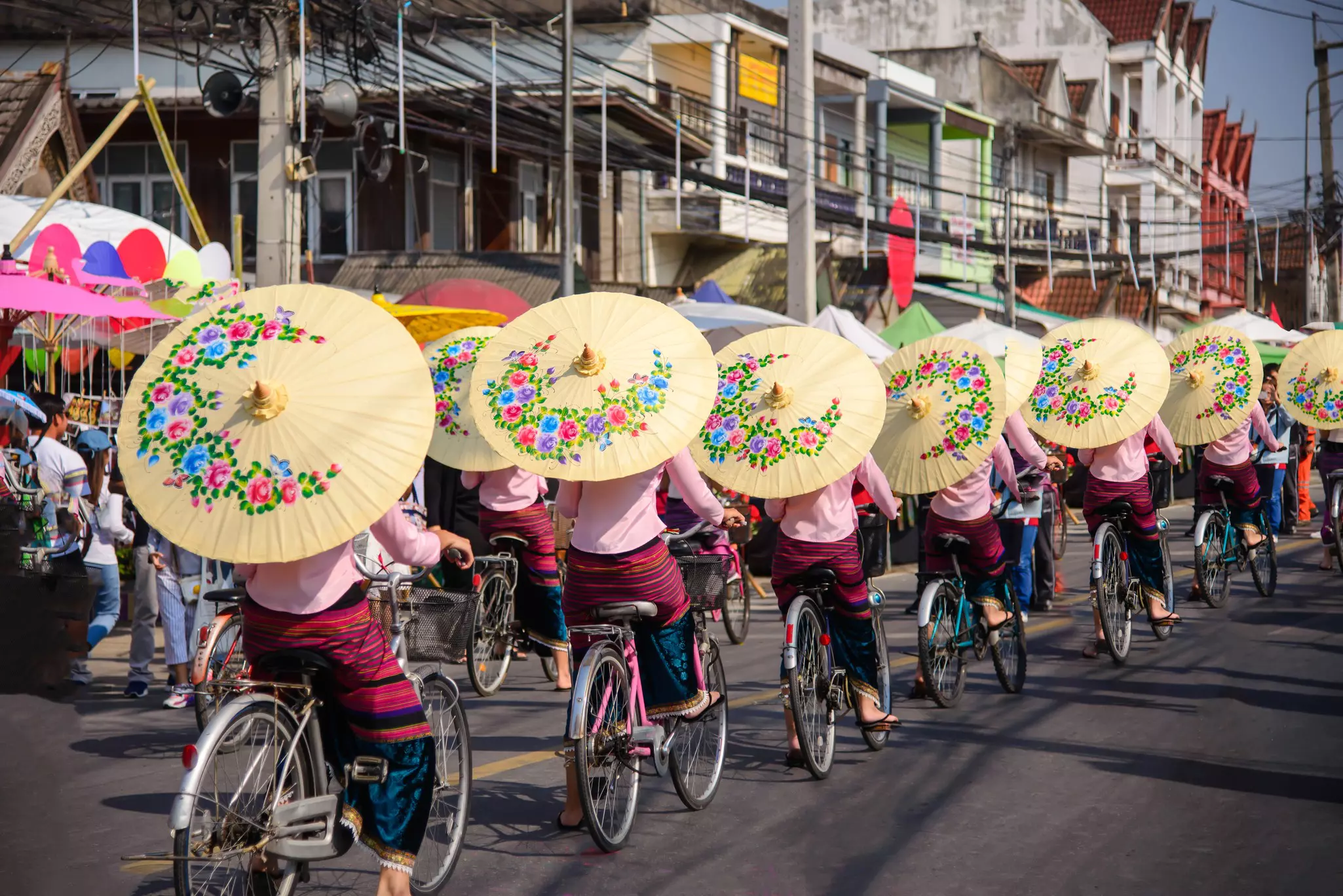 Women holding beautiful umbrellas and cycling during the Bo Sang Umbrella Festival