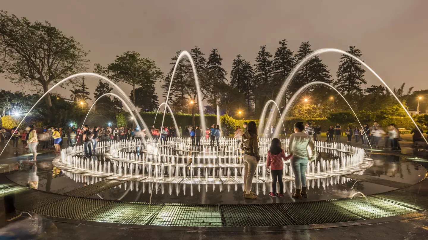 People stand in a park by an elaborate fountain with dozens of jets.