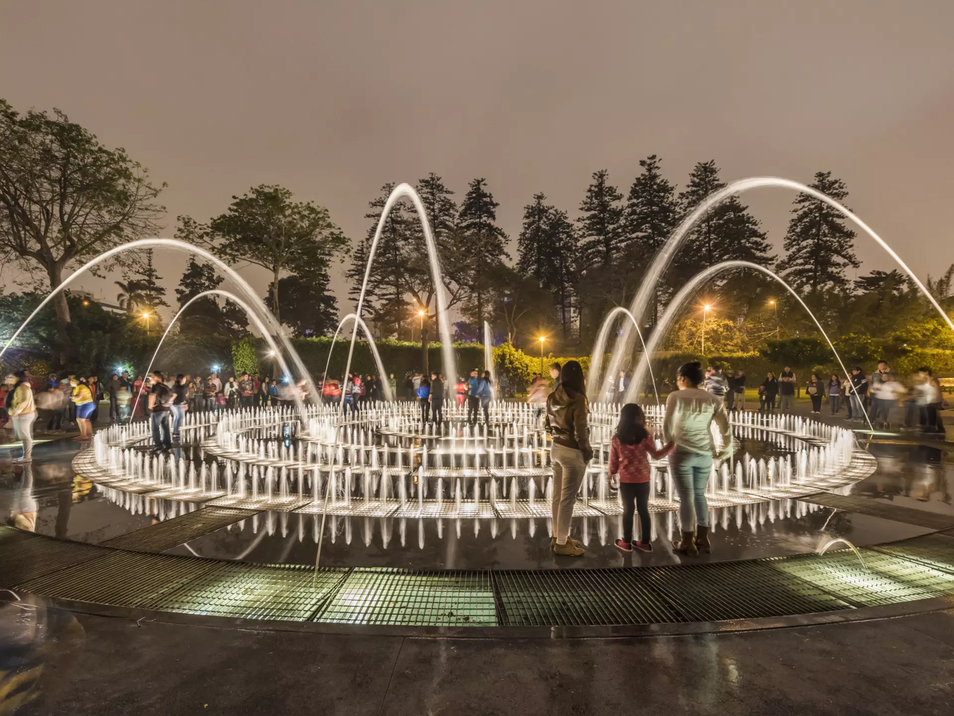People stand in a park by an elaborate fountain with dozens of jets.