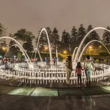 People stand in a park by an elaborate fountain with dozens of jets.