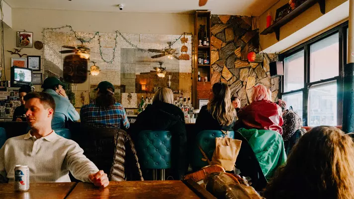 patrons sit on green leather bar stools watching a tiny television at a bar