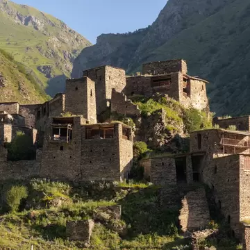Cluster of medieval slate-stone towers with wooden balconies on a grassy slope beneath steep Caucasus mountainsides