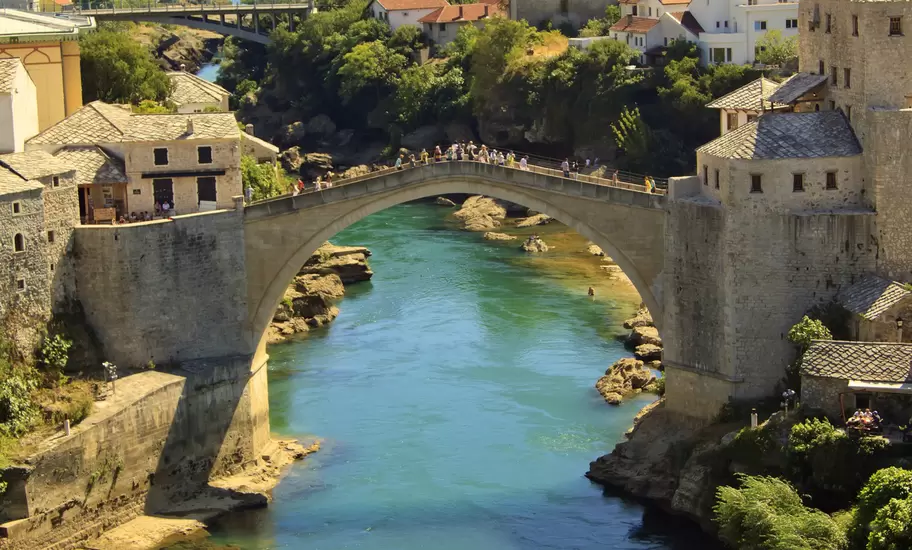 Stari Most, the arched Old Bridge in Mostar, spanning the green Neretva River between stone towers, with hills beyond
