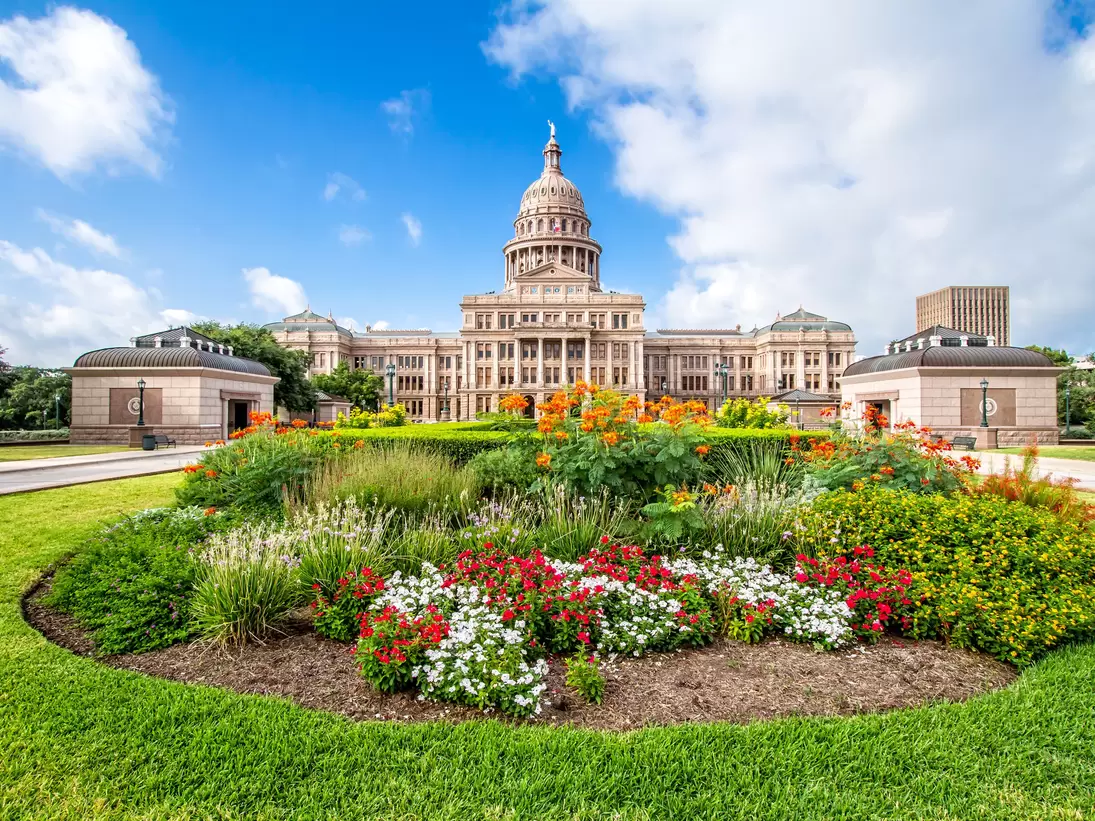 The Texas State Capitol with flower garden. It was completed in 1888 in Downtown Austin. It contains the offices and chambers of the Texas Legislature and the Office of the Governor.